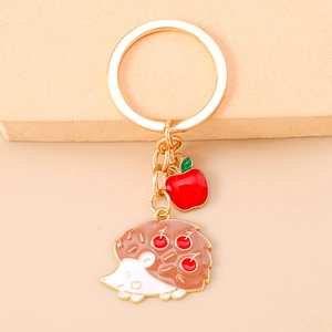 Detail of metal keychain with red apple and cute hedgehog pendant with cherry patterns