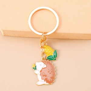 Close-up of golden keychain with enamel hedgehog and yellow corn cob bag pendants
