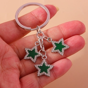 Green enamel star keychain with sparkling white rhinestones held against a pink backdrop
