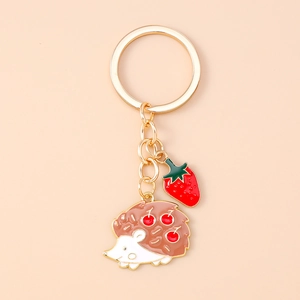 Close-up of golden keychain featuring a cartoon hedgehog with cherry and strawberry charms