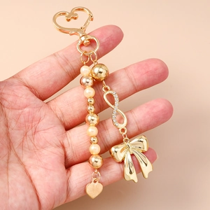 Golden heart keychain with pearl beads, infinity symbol, and bow charm held in hand