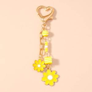 Detail of yellow daisy keychain with golden heart clasp and beaded charms on beige