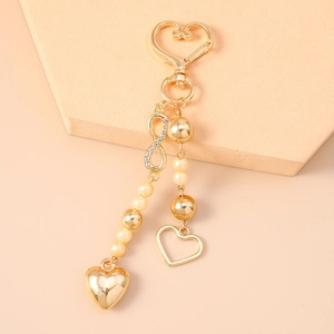 Detail of a golden heart keychain with faux pearls, infinity symbol, and crystal accents