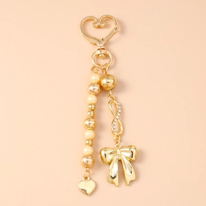 Detail of gold bow keychain with faux pearls, infinity charm, and heart clasp