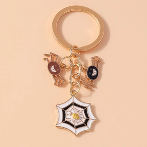 Detailed close-up of Halloween keychain featuring gold spider and cobweb charms on pink base