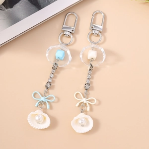 Détail du porte-clés fleur en coquillage avec strass et ruban sur fond beige uni