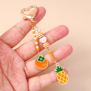 Nahaufnahme von goldenem Herz-Schlüsselanhänger mit Emaille-Ananas und Kaki-Anhängern