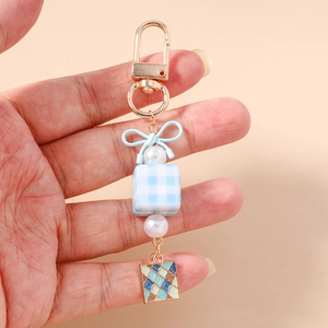 Blue bow keychain with checkerboard cube and pearl charm held by a person