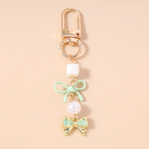 Détail d'un porte-clés en perles avec nœud vert et fermoir mousqueton doré sur fond rose