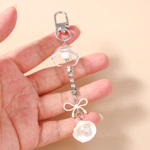 Détail d'un porte-clés avec chaîne en strass, nœud en résine blanche et pendentif perle