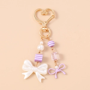 Close-up of a pearl bow keychain with purple striped beads and golden heart clasp