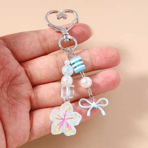 Dettaglio di un portachiavi con perline, fiocco blu e fiore tenuto in mano su sfondo beige