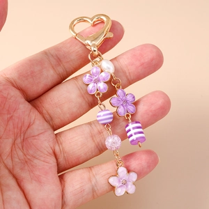 Detailansicht lila Emailleblumen und Herzkarabiner an einem goldenen Schlüsselanhänger