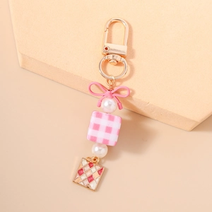 Detail of pink bow and checkered square charms on a stylish golden keychain pendant