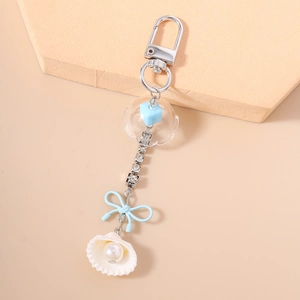 Détail d'un porte-clés nautique avec nœud bleu clair, coquillage blanc et perle d'imitation