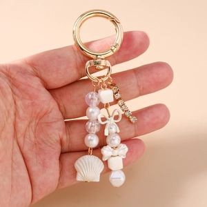 Détail du porte-clés avec pendentif coquillage, perles, nœud blanc et chaîne en strass