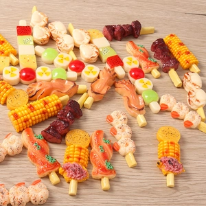 Macro shot of miniature resin food charms including grilled shrimp and corn on wooden background