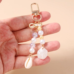 Close-up of golden beaded keychain with pearl bow and natural cowrie shell charms