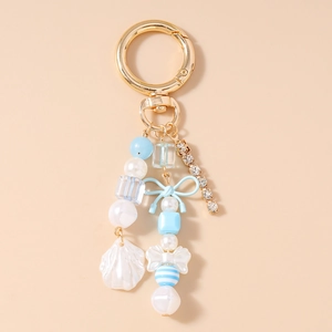 Détail d'un porte-clés perlé avec nœud bleu, breloque coquillage et chaîne strass