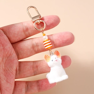 Détail d'un porte-clés chat en peluche avec flocage blanc et perles nacrées