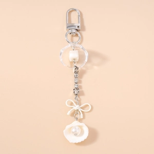 Détail du porte-clés avec nœud blanc, chaîne en strass, coquillage et pendentif perle