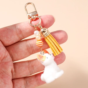 Détail de porte-clés chien en peluche blanche avec perles, pompon jaune et fermoir doré