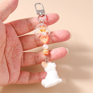 Détail d'un lapin floqué blanc avec perle de cœur orange et breloques à pampilles