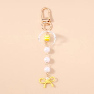 Détail d'un porte-clés à nœud jaune avec perles et anneau acrylique sur fond rose