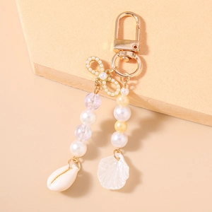 Golden keychain with bow, faux pearls, sea shells and nautical beads on a beige base
