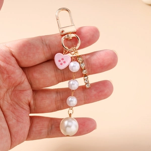 Dettaglio di un portachiavi di perle con ciondolo a cuore rosa e catena di strass in mano