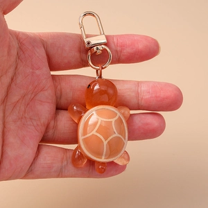 Detail of orange resin turtle keychain with gold metal clasp held in hand