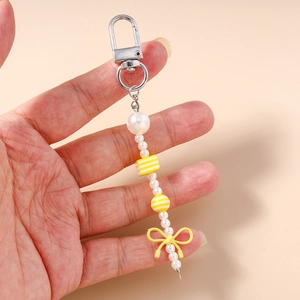 Detail of beaded keychain with white pearls and a yellow ribbon bow decoration