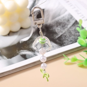 Gros plan d'un porte-clés méduse avec nœud vert, perles et couvercle transparent