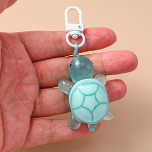 Close-up of a blue resin turtle keychain with a white swivel clasp held by a hand