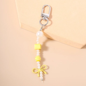 Detail of beaded keychain featuring white imitation pearls and a yellow ribbon bow pendant