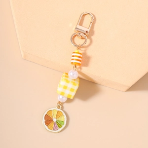 Detail view of fruit keychain with lemon slice charm, pearls, and yellow checkered cube