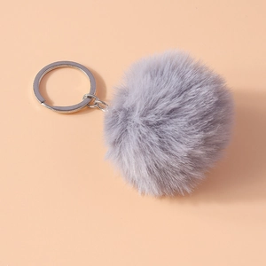 Detail of soft grey faux fur pompom keychain with silver metal ring on peach background