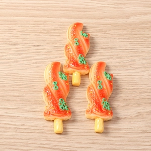 Detailed macro view of resin food charms shaped like grilled skewers with sauce and scallions