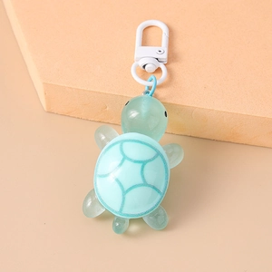 Detail of mint green 3D turtle keychain with blue geometric shell on orange stand