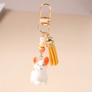 Détail d'un porte-clés chiot blanc en peluche avec pompon jaune et fermoir doré