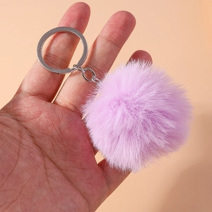 Close-up of a fluffy 8cm purple faux fur pompom keychain held against a solid orange background