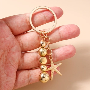 Détail d'un porte-clés doré avec étoile de mer et perles tenu dans la main
