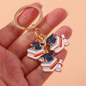 Close-up of graduation keychain featuring metal book, cap, and diploma charms held by hand