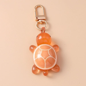 Detail shot of orange resin turtle keychain with gold lobster clasp on pink background