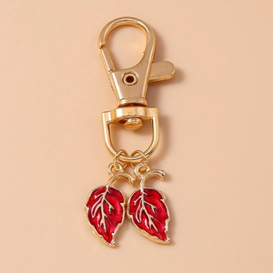 Détail d'un porte-clés feuille dorée avec gouttes d'émail rouge et fermoir mousqueton