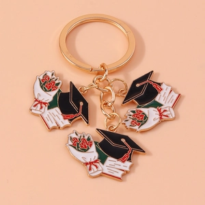 Golden graduation keychain featuring a black mortarboard hat, red roses, and diploma charms