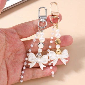 Handheld view of Y2K pearl bow keychains with gold and silver metal lobster clasps