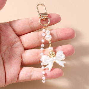 Detail of beaded Y2K pearl keychain with a white bow and golden lobster clasp