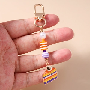 Handheld detail of a colorful cake pendant keychain with striped beads and a white pearl