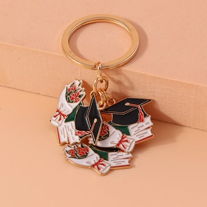 Detail of graduation keychain with gold metal cap and diploma charms on a soft textured stand